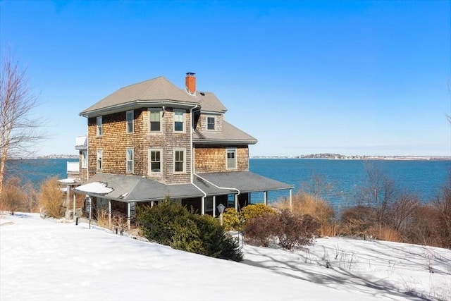 snow covered property featuring a water view and a chimney