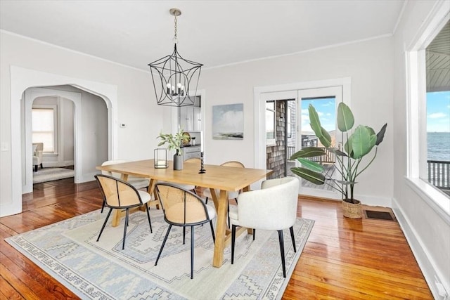 dining space featuring arched walkways, crown molding, light wood finished floors, baseboards, and a chandelier