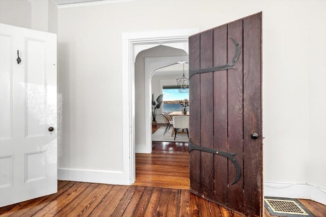 hall featuring visible vents, baseboards, wood finished floors, and a chandelier