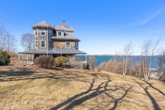 rear view of property with covered porch, a lawn, and a chimney