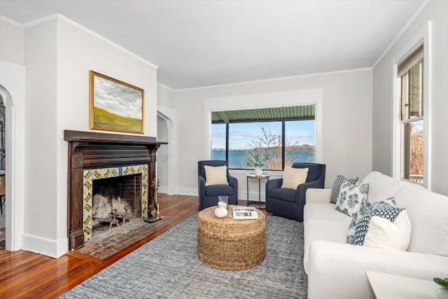 living area featuring ornamental molding, a tiled fireplace, wood finished floors, arched walkways, and baseboards