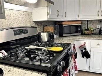 kitchen with light stone countertops, appliances with stainless steel finishes, white cabinetry, decorative backsplash, and ventilation hood