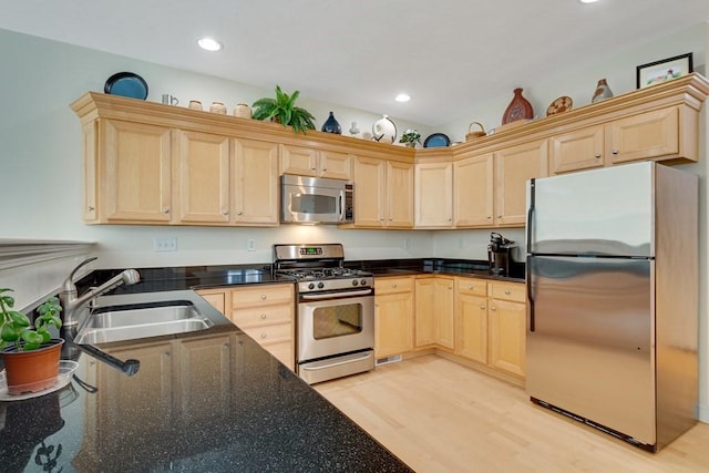 kitchen with light hardwood / wood-style flooring, sink, appliances with stainless steel finishes, dark stone countertops, and light brown cabinets