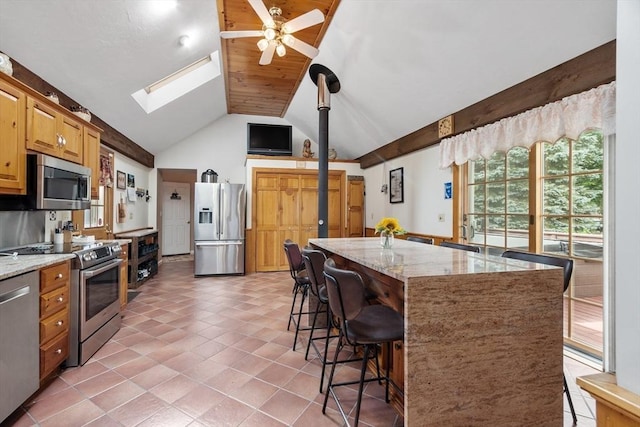 kitchen featuring a breakfast bar area, a center island, ceiling fan, stainless steel appliances, and light stone countertops