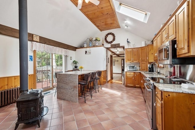 kitchen with sink, a breakfast bar, a skylight, stainless steel appliances, and a wood stove