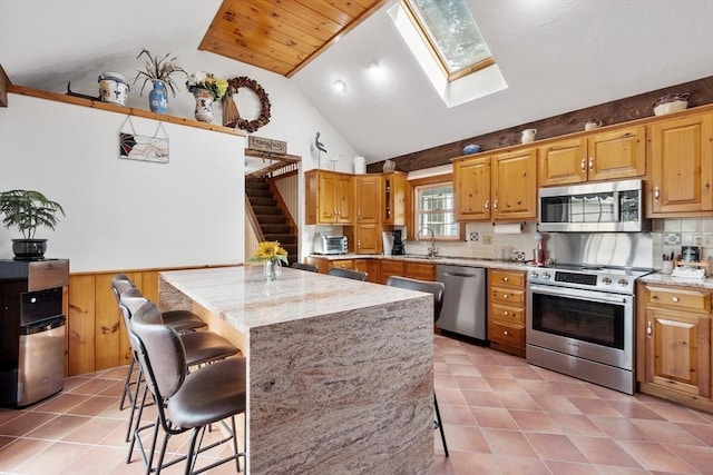 kitchen with sink, light stone counters, a kitchen breakfast bar, a kitchen island, and stainless steel appliances