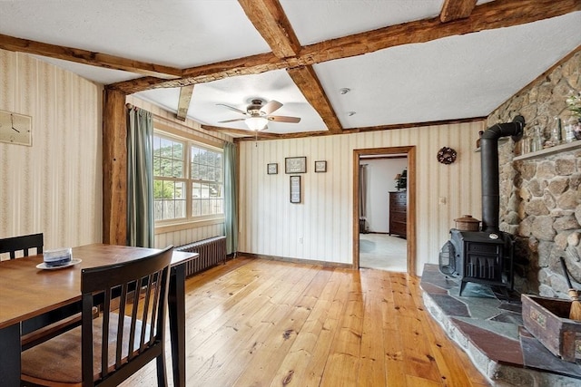 interior space with radiator, ceiling fan, beamed ceiling, and a wood stove