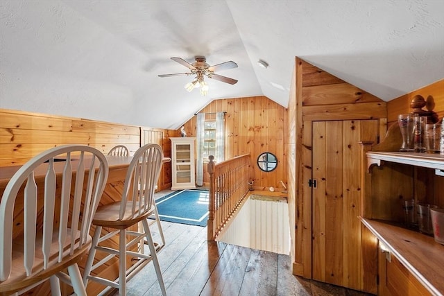 interior space featuring ceiling fan, wood-type flooring, vaulted ceiling, and wood walls