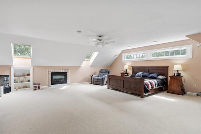 bedroom with a tiled fireplace, lofted ceiling with skylight, light colored carpet, and ceiling fan