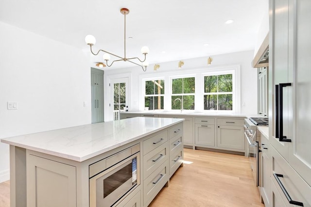 kitchen with built in appliances, a center island, light wood-type flooring, a chandelier, and light stone counters