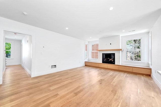 unfurnished living room with a tiled fireplace, baseboards, and light wood-style flooring