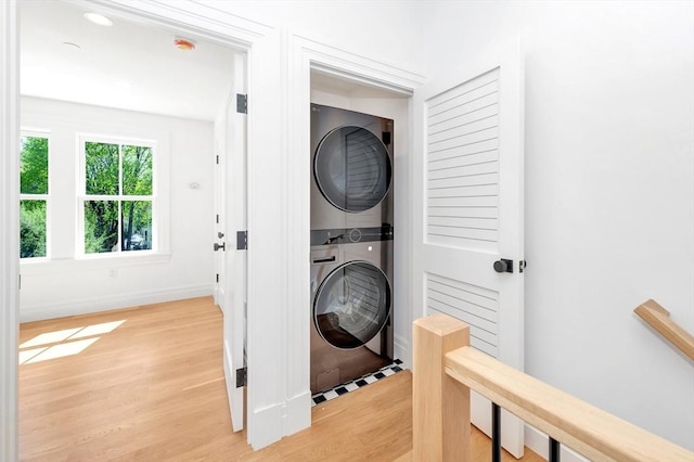 laundry room featuring laundry area, baseboards, stacked washer / dryer, and light wood-type flooring