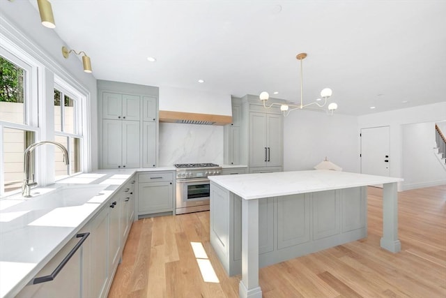 kitchen featuring a kitchen island, backsplash, high end stove, a sink, and light wood-style floors
