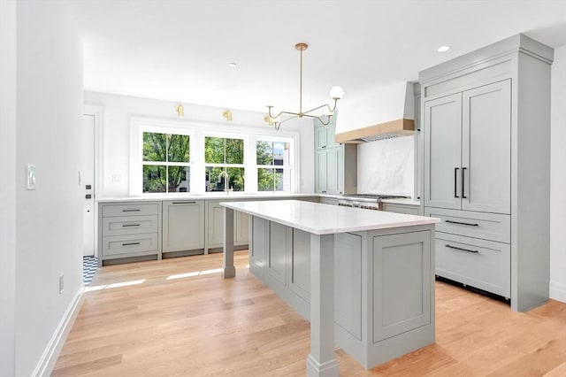 kitchen with gray cabinetry, custom range hood, light wood-style flooring, and a notable chandelier