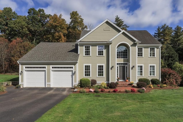 colonial house with a front lawn, an attached garage, driveway, and a shingled roof