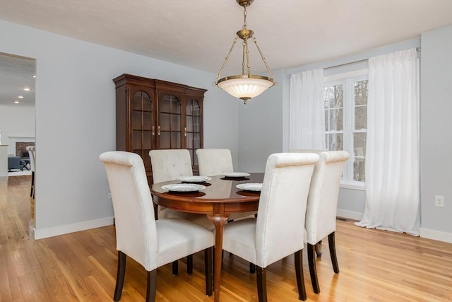 dining space featuring a fireplace, plenty of natural light, baseboards, and light wood-type flooring