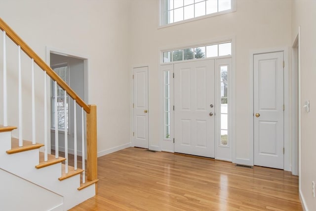 entryway featuring visible vents, stairway, light wood-style floors, baseboards, and a towering ceiling