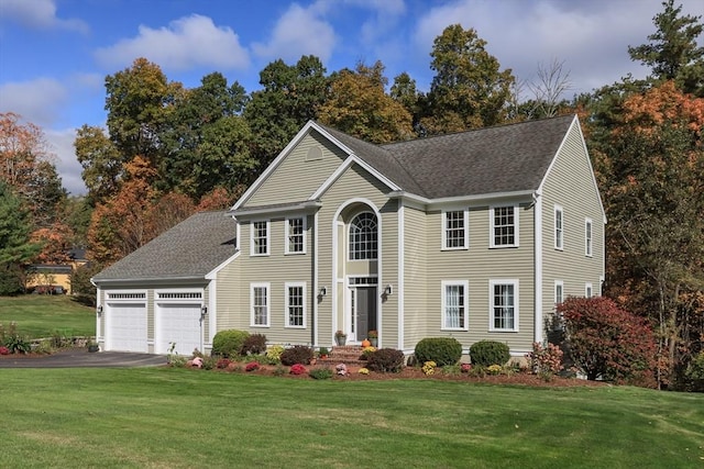 colonial-style house featuring a garage, driveway, a front yard, and roof with shingles