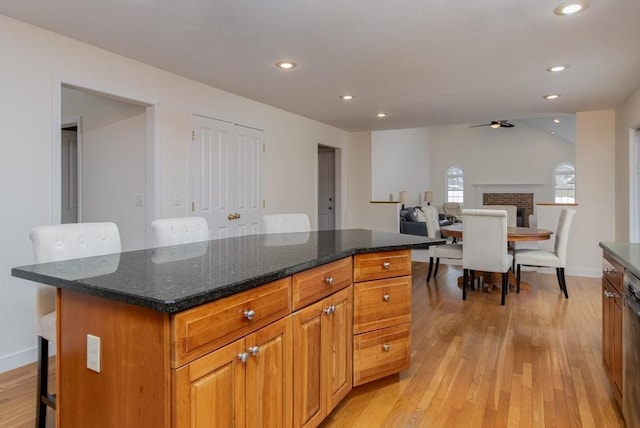 kitchen with a breakfast bar area, a brick fireplace, recessed lighting, and light wood-style flooring