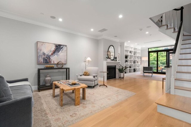 living room with built in features, light hardwood / wood-style floors, and crown molding