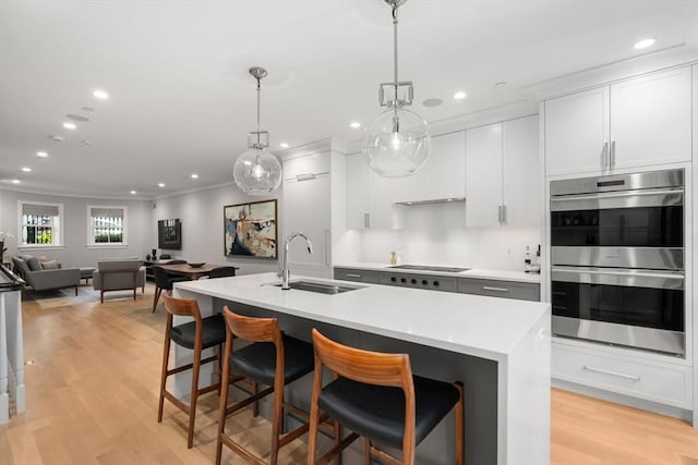 kitchen with sink, white cabinetry, hanging light fixtures, a center island with sink, and stainless steel double oven