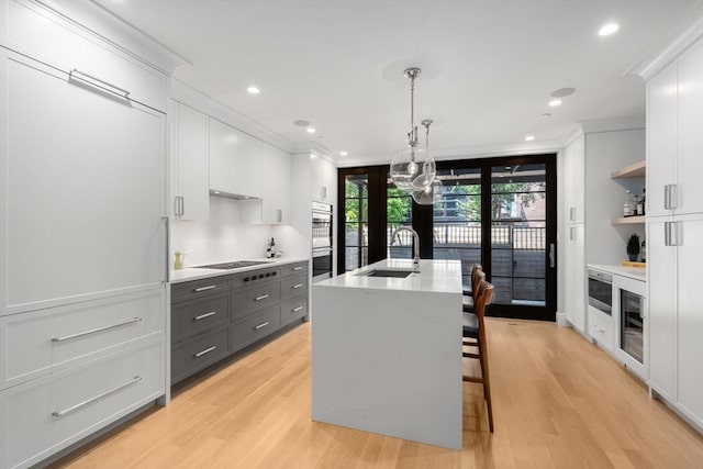 kitchen with sink, gray cabinets, white cabinetry, a kitchen island with sink, and decorative light fixtures