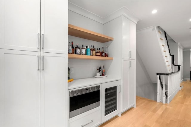 bar with paneled built in fridge, light hardwood / wood-style floors, white cabinets, and beverage cooler