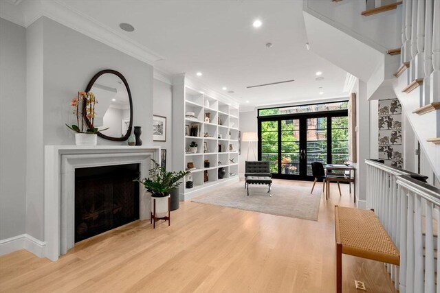 living room with built in shelves, light hardwood / wood-style floors, crown molding, and french doors