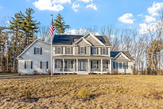 colonial home with solar panels, a porch, and a front yard