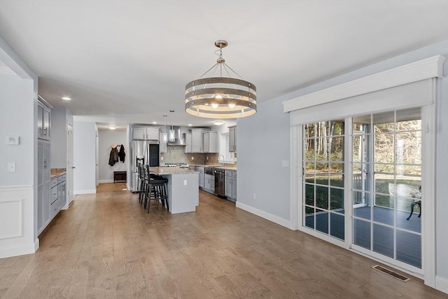 kitchen with a breakfast bar, stainless steel appliances, pendant lighting, a center island, and light hardwood / wood-style floors