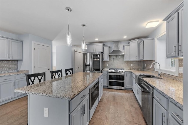 kitchen with wall chimney exhaust hood, light hardwood / wood-style floors, a breakfast bar, a kitchen island, and appliances with stainless steel finishes