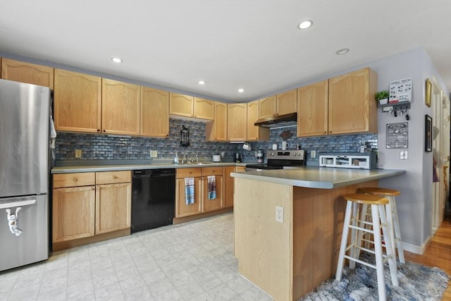 kitchen with a kitchen bar, a peninsula, under cabinet range hood, stainless steel appliances, and decorative backsplash