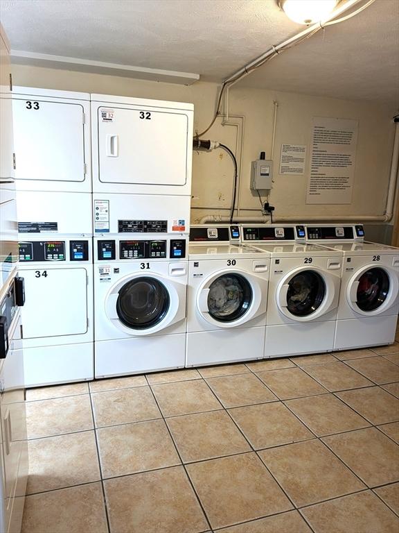 washroom with stacked washer / dryer, washing machine and dryer, and light tile patterned floors