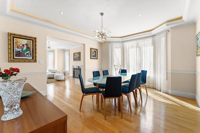 dining area with a notable chandelier, light wood-style flooring, a tiled fireplace, a tray ceiling, and crown molding