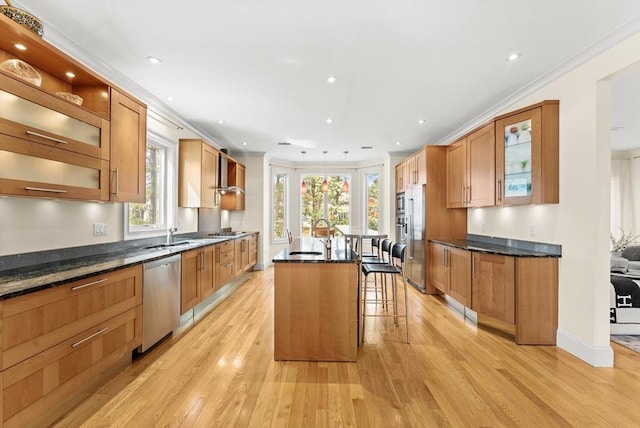 kitchen with a center island with sink, ornamental molding, light wood-style flooring, a kitchen breakfast bar, and stainless steel appliances