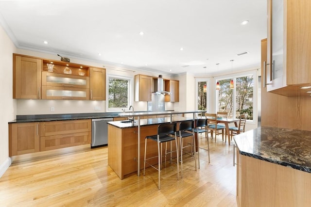 kitchen featuring light wood finished floors, stainless steel dishwasher, a breakfast bar area, wall chimney exhaust hood, and crown molding