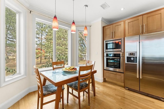 kitchen with light wood-type flooring, visible vents, ornamental molding, decorative light fixtures, and stainless steel appliances