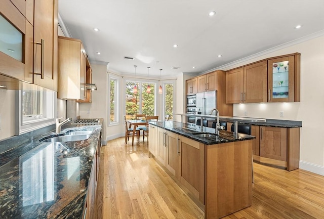 kitchen featuring a center island with sink, appliances with stainless steel finishes, ornamental molding, and a sink