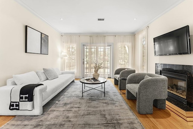 living area featuring wood finished floors, a fireplace, visible vents, and ornamental molding