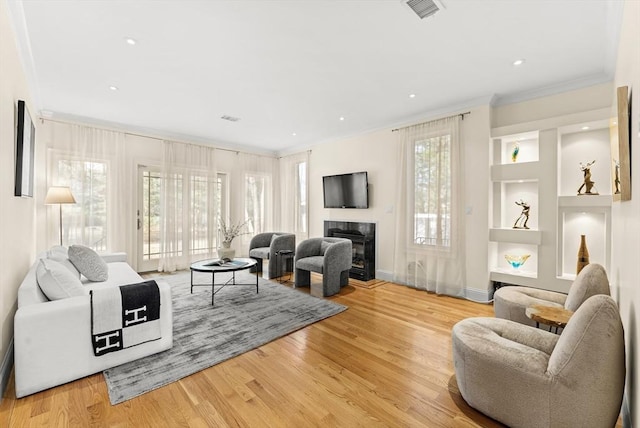 living room with a glass covered fireplace, plenty of natural light, visible vents, and wood finished floors