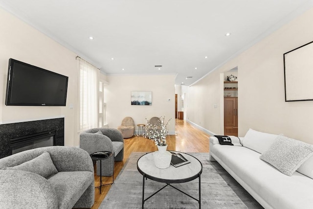 living room featuring recessed lighting, a premium fireplace, wood finished floors, and crown molding