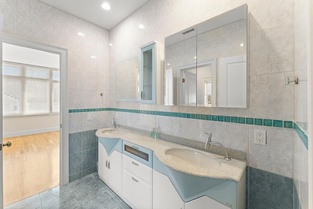 bathroom featuring double vanity, visible vents, tile walls, and a sink