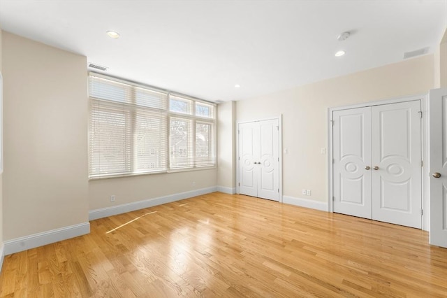 unfurnished bedroom with visible vents, light wood-style flooring, baseboards, and multiple closets