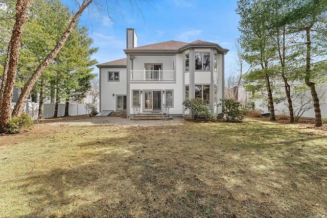 back of property featuring fence, entry steps, a lawn, a chimney, and a balcony