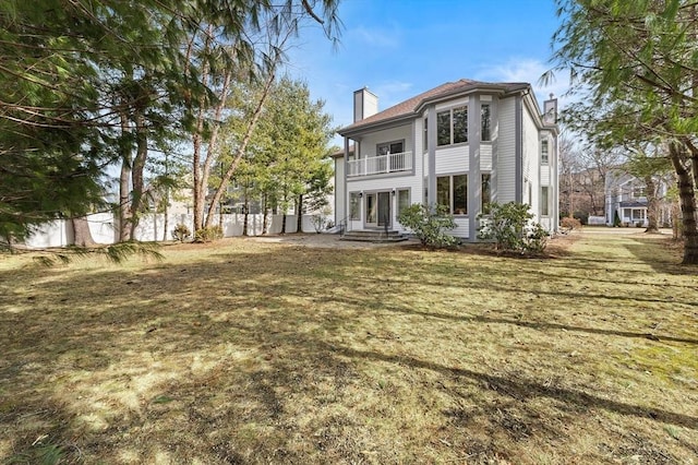 rear view of property featuring a yard, a chimney, a balcony, and fence