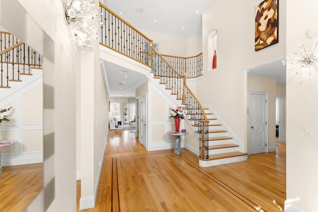 entryway with wood finished floors, stairway, crown molding, a decorative wall, and a towering ceiling