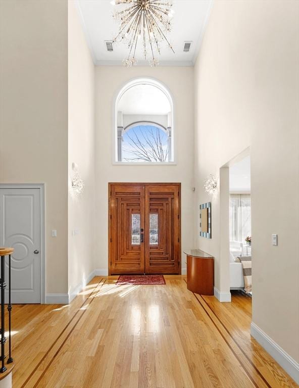 foyer with visible vents, baseboards, a high ceiling, wood finished floors, and a notable chandelier