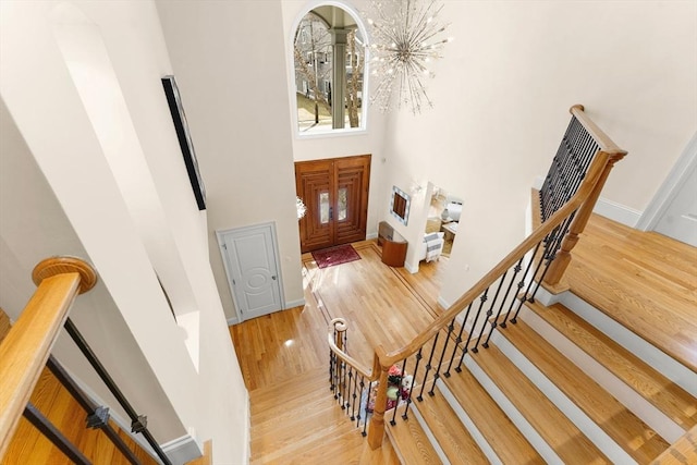 stairway featuring wood finished floors, baseboards, a towering ceiling, and a chandelier