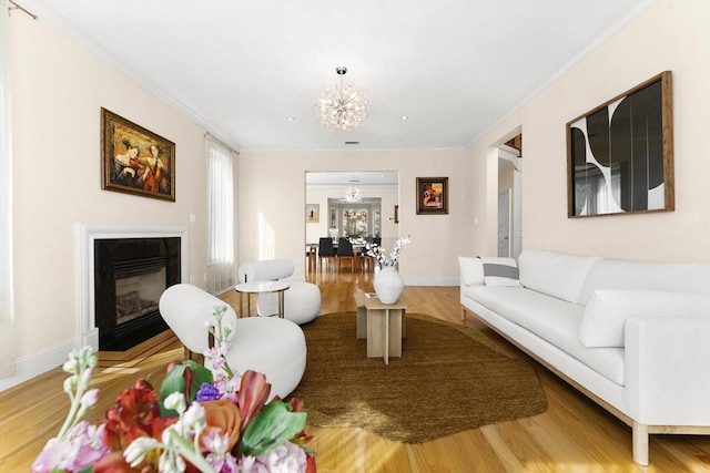 living room with wood finished floors, baseboards, a glass covered fireplace, crown molding, and a notable chandelier