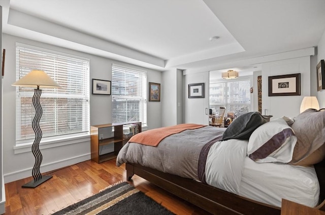 bedroom featuring hardwood / wood-style flooring, multiple windows, and a tray ceiling